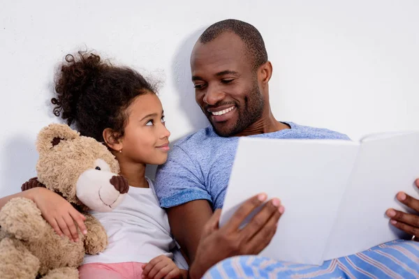 Afrikanisch-amerikanischer Vater hält Buch und schaut Tochter zu Hause an — Stockfoto