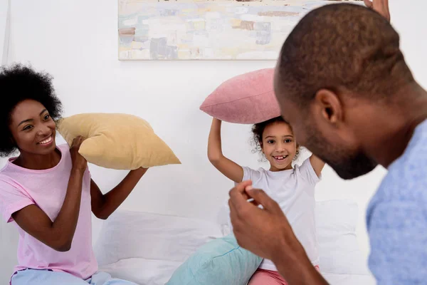 Африканские американские родители и дочь играют с подушками в спальне — стоковое фото