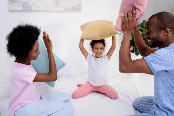 African american parents and daughter having fun with pillows at home — Stock Photo