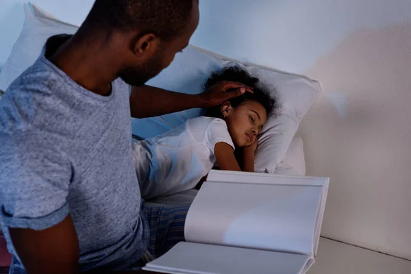 Afro-américain père tenant livre et palming sommeil fille — Photo de stock