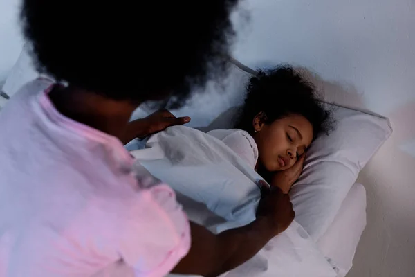 African american mother covering sleeping daughter with blanket at home — Stock Photo