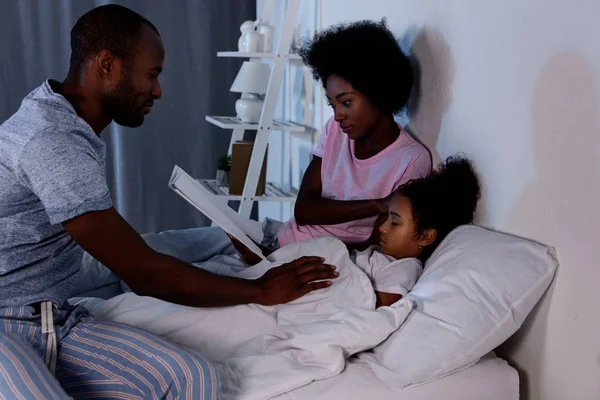 Afroamericanos padres leyendo hija antes de dormir en casa - foto de stock