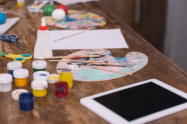 Pinturas de póster para huevos de Pascua y tableta en mesa de madera - foto de stock