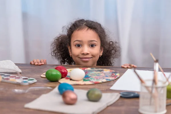 Entzückendes afrikanisch-amerikanisches Kind blickt in die Kamera am Tisch mit Ostereiern — Stockfoto