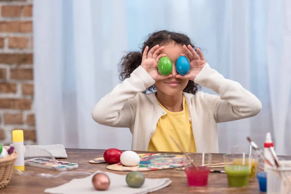Criança americana africana se divertindo e cobrindo os olhos com ovos de páscoa pintados — Fotografia de Stock