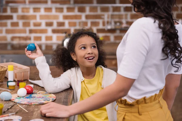 Cropped image of african american daughter having fun with painted easter egg — Stock Photo