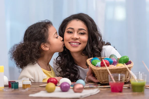 Африканская американская дочь целует счастливую мать возле окрашенных пасхальных яиц — стоковое фото