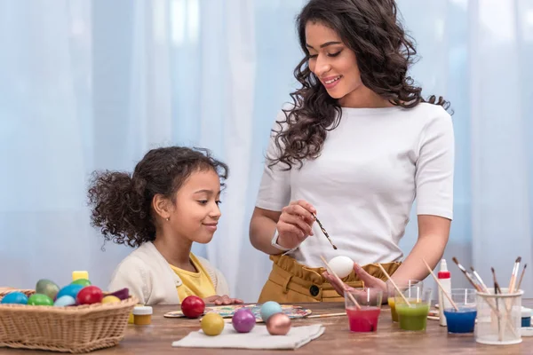 Madre afroamericana enseñando a su hija a pintar huevos de Pascua - foto de stock