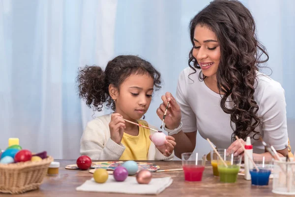 Feliz africano americano madre y hija pintura Pascua huevos - foto de stock