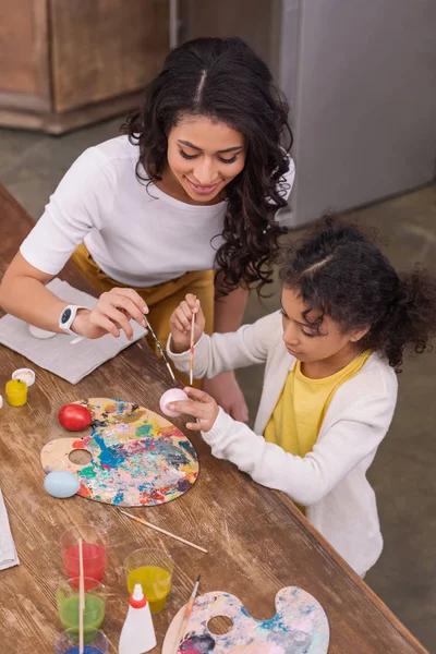Vista de ángulo alto de la madre afroamericana y la hija pintando huevos de Pascua - foto de stock
