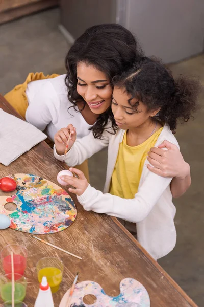 Alto angolo vista di afro americano madre abbracciare figlia mentre lei pittura uova di Pasqua — Foto stock