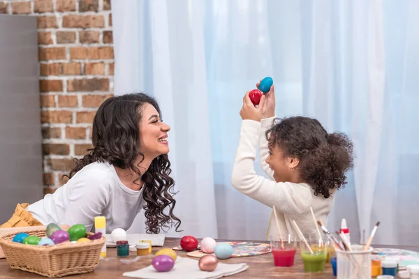 Riéndose africano americano madre e hija tener divertido con pintado Pascua huevos - foto de stock