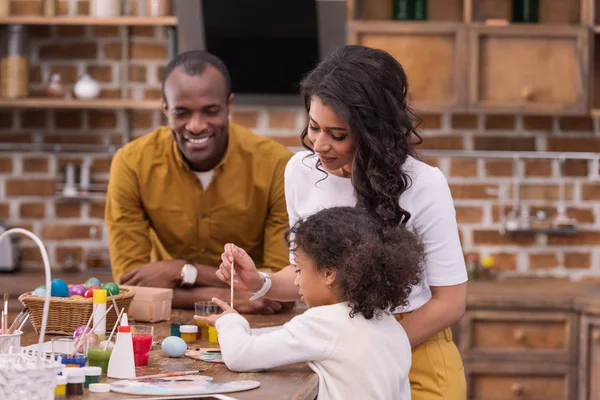 Padres afroamericanos y su hija pintando huevos de Pascua - foto de stock