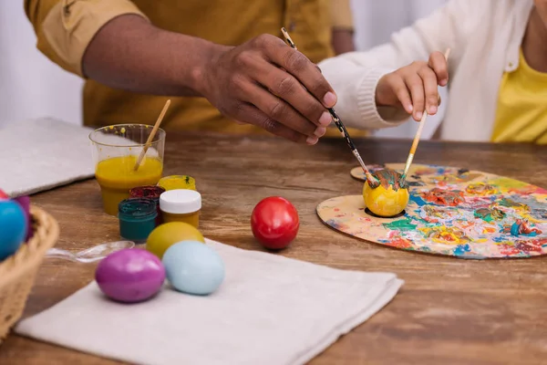 Cropped image of african american father and daughter painting easter eggs with poster paints — Stock Photo