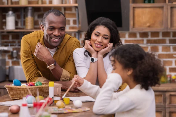 Felice afro-americano genitori guardando come figlia pittura uova di Pasqua — Foto stock