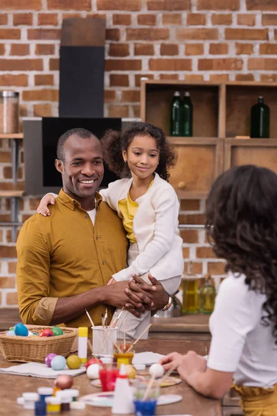 African american father carrying daughter, mother standing at table with easter eggs — Stock Photo