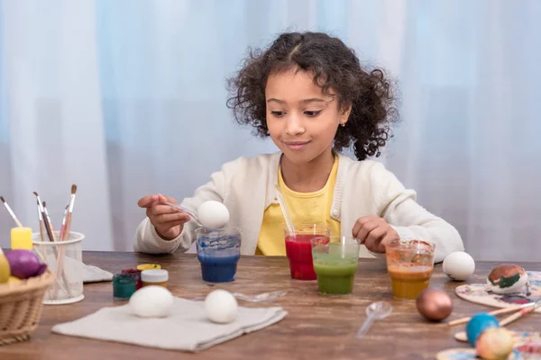 Cheerful african american child painting easter eggs in glasses with paints — Stock Photo