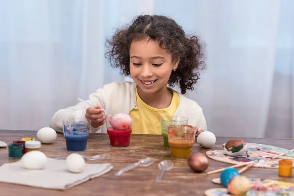 Fröhliches afrikanisch-amerikanisches Kind bemalt Ostereier in Gläsern mit Farben — Stockfoto