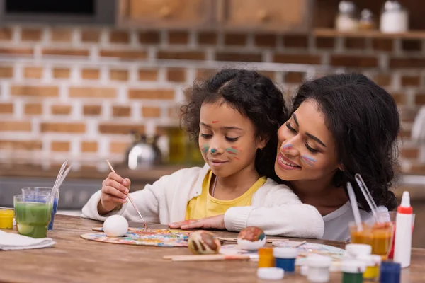 Afro-americana mãe olhando como filha pintura Páscoa ovo — Fotografia de Stock