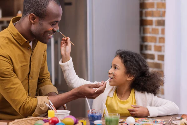 Afro-americano pai e filha se divertindo e pintando rostos, conceito de Páscoa — Fotografia de Stock