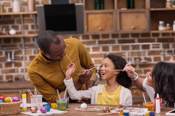 Счастливые африканские американские родители и дочь веселятся и рисуют лица — стоковое фото