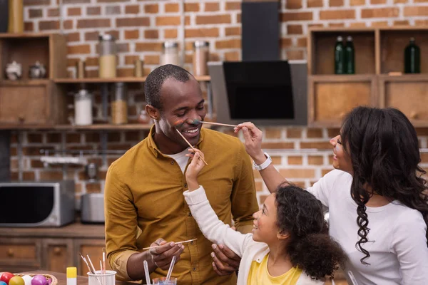 Heureux afro-américain mère et fille peinture père visage avec des peintures, concept de Pâques — Photo de stock