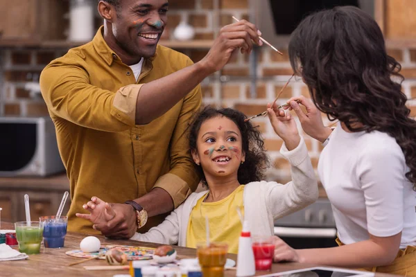 Africanos americanos padres y hija tener divertido mientras pintura Pascua huevos - foto de stock