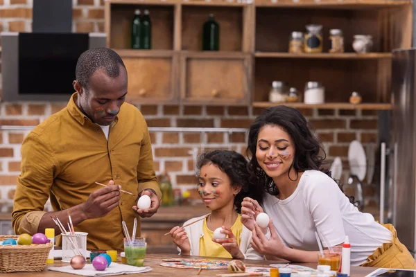Souriants afro-américains parents et fille peignant des œufs de Pâques ensemble sur la cuisine — Photo de stock