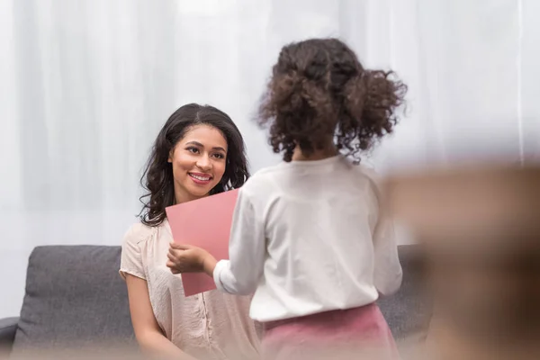 Rückseite der afrikanisch-amerikanischen Tochter überreicht der Mutter am Muttertag eine Grußkarte — Stockfoto