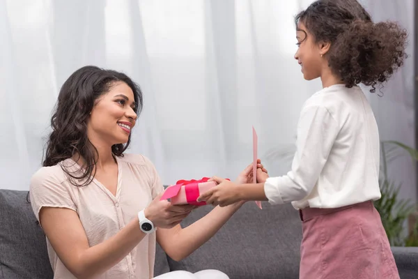 Vista lateral de la hija afroamericana que presenta regalos a la madre en el día de la madre - foto de stock