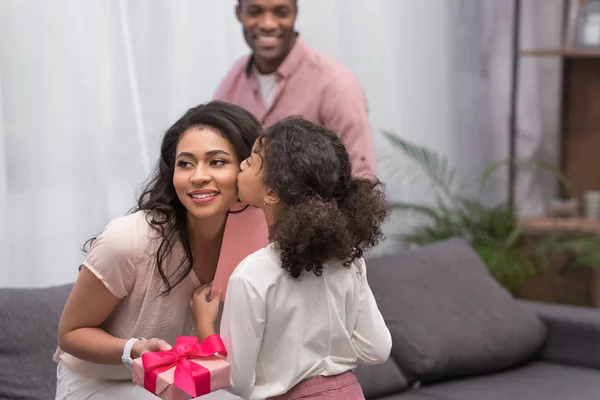 Hija afroamericana besando a la madre y presentándole regalos en el día de la madre - foto de stock