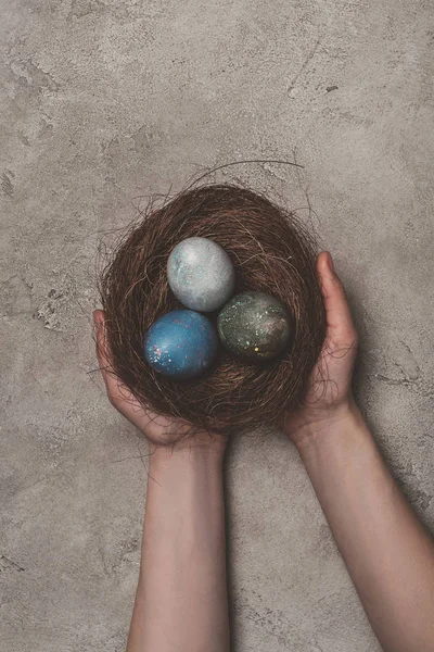 Cropped view of man holding nest with easter eggs on concrete surface — Stock Photo