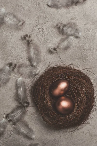 Top view of golden easter eggs in nest with feathers on concrete surface — Stock Photo