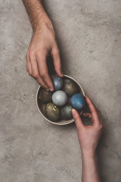 Vista recortada de pareja con tazón de huevos de Pascua en la superficie de hormigón - foto de stock