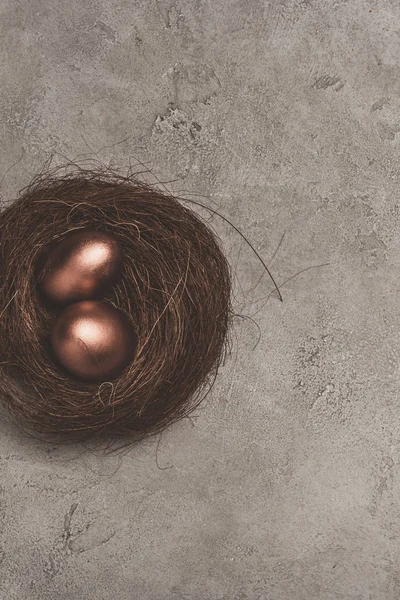 Vista superior de huevos de Pascua dorados en el nido en la superficie de hormigón - foto de stock