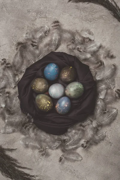 Vista superior de los huevos de Pascua en el nido con plumas en la superficie de hormigón - foto de stock