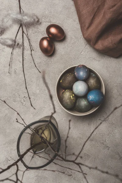 Top view of painted easter eggs in bowl and willow branches in vase on concrete surface — Stock Photo