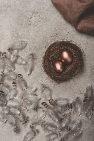 Top view of golden easter eggs in nest on concrete surface with feathers — Stock Photo
