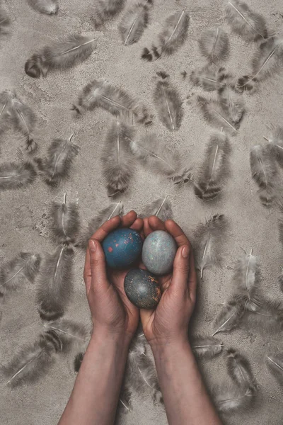 Cropped view of man holding easter eggs on concrete surface with feathers — Stock Photo