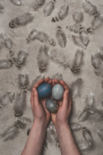 Vista ritagliata dell'uomo che tiene uova di Pasqua su una superficie di cemento con piume — Foto stock