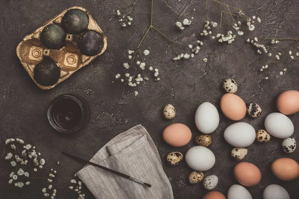 Top view of painted eggs in golden tray, quail and chicken eggs, paint and brush on cloth and concrete surface, Easter decorations — Stock Photo