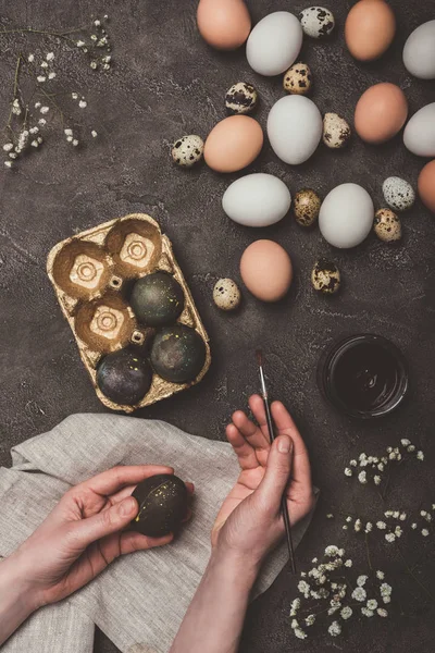 Vista recortada del hombre pintando huevos de Pascua y poniéndolos en bandeja, flores, codornices y huevos de pollo cerca — Stock Photo