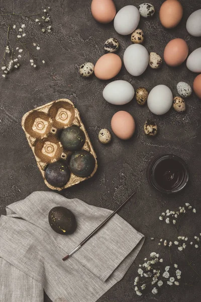 Vista dall'alto di uova di Pasqua in vassoio d'oro, uova di quaglia e di pollo, vernice e pennello su stoffa e superficie di cemento — Foto stock