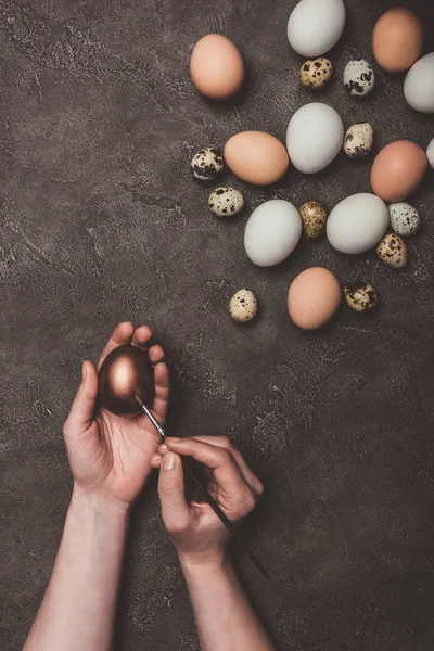 Vista recortada del hombre pintando huevo de Pascua dorado, codorniz y huevos de pollo cerca - foto de stock