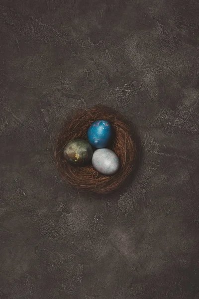 Top view of nest with three painted easter egg on concrete table — Stock Photo
