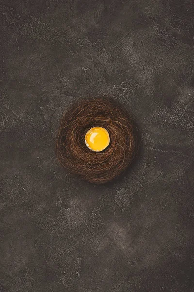 Vista superior de ovo quebrado com gema de ovo no ninho na superfície de concreto — Fotografia de Stock
