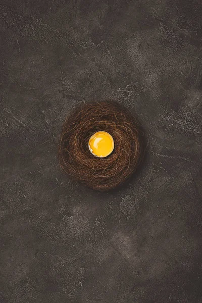 Top view of broken egg with yolk in nest on concrete surface — Stock Photo