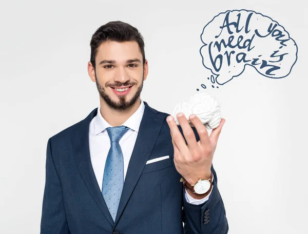 Joven hombre de negocios sosteniendo el modelo de cerebro con la inscripción todo lo que necesita es cerebro y sonriendo a la cámara aislado en gris - foto de stock