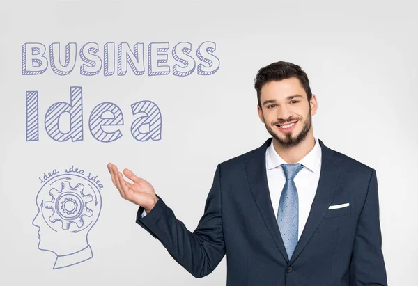 Handsome young businessman showing business idea inscription  and smiling at camera isolated on grey — Stock Photo