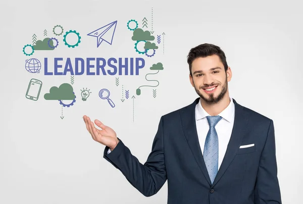 Handsome young businessman showing leadership icons and smiling at camera isolated on grey — Stock Photo